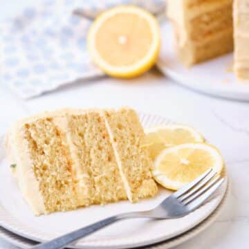 A slice of lemon curd cake on a plate with the lemon curd layer cake in the background.