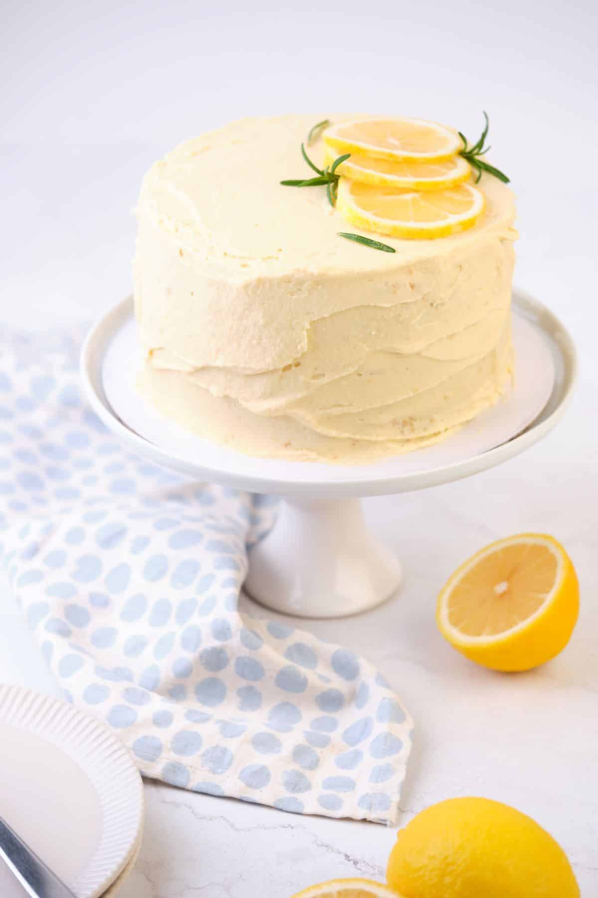 A lemon layer cake on a cake pedestal decorated with fresh lemons.