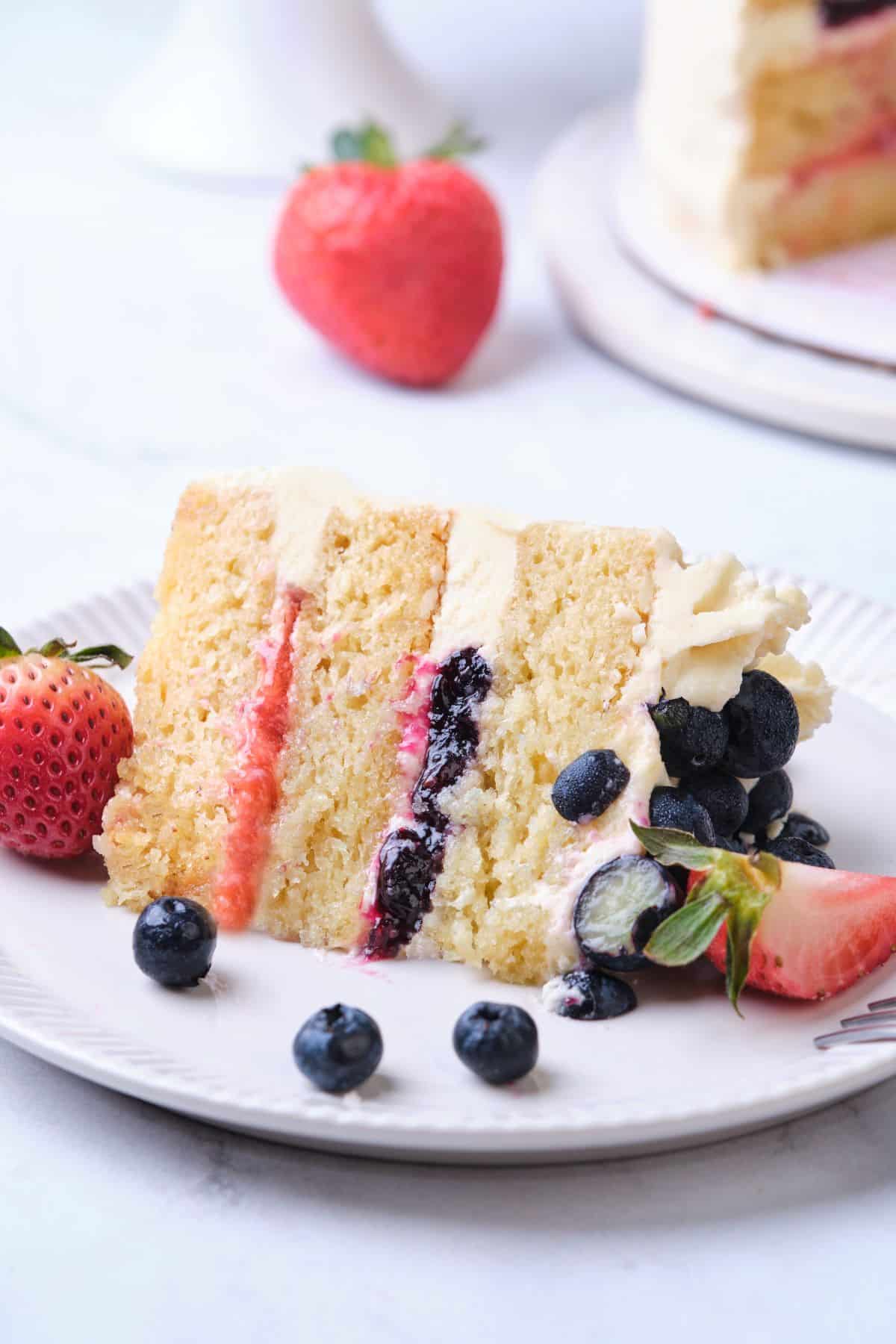 A Vanilla Strawberry Blueberry Layer Cake Slice on a plate.