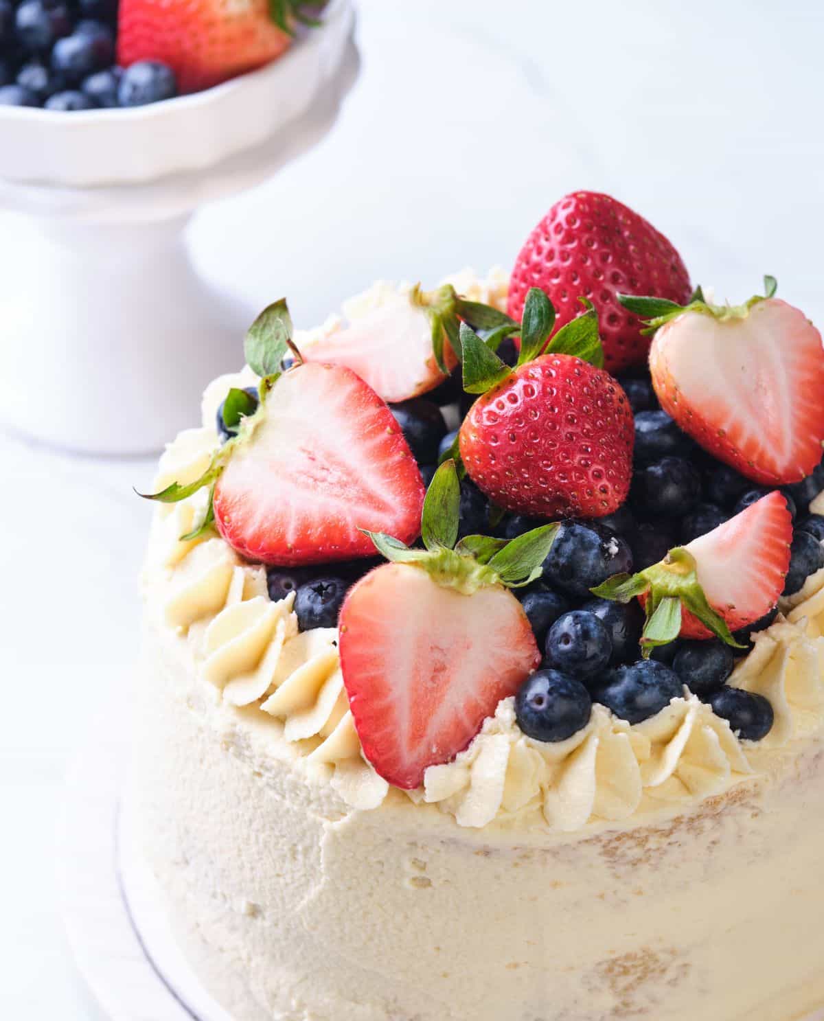 A layer cake topped with fresh strawberries and fresh blueberries.