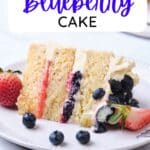 A slice of moist vanilla cake with one layer of strawberry filling and one layer of blueberry filling, topped with fresh strawberries and fresh blueberries.