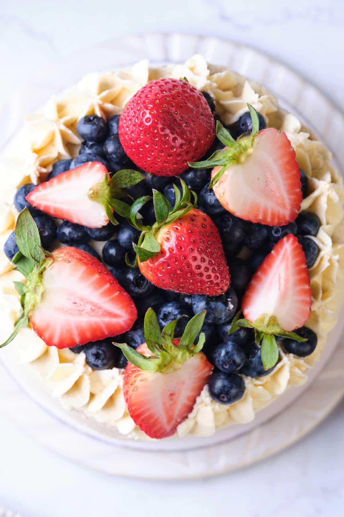 An overhead shot of a layer cake topped with a lot of strawberries and blueberries.