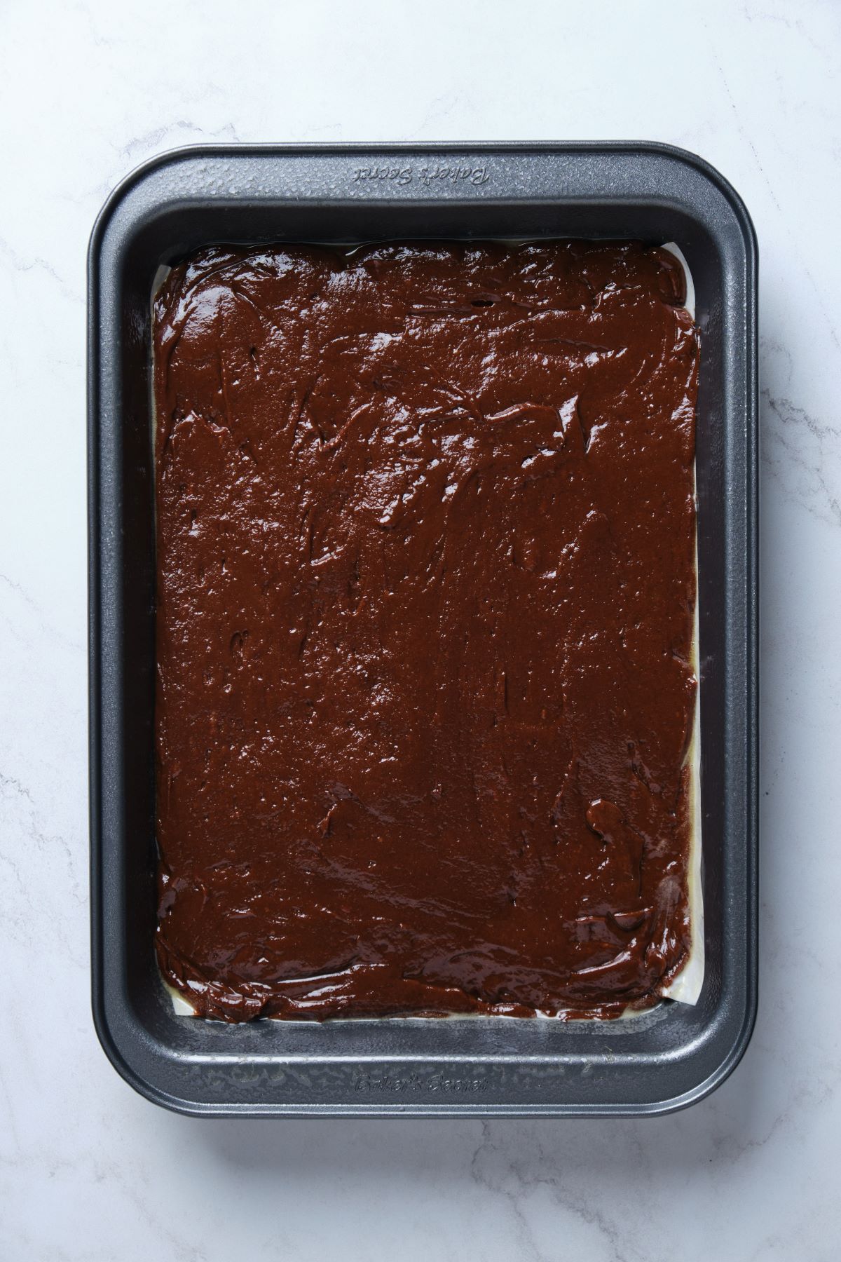 The chocolate fudge cake batter spread into a cake pan.