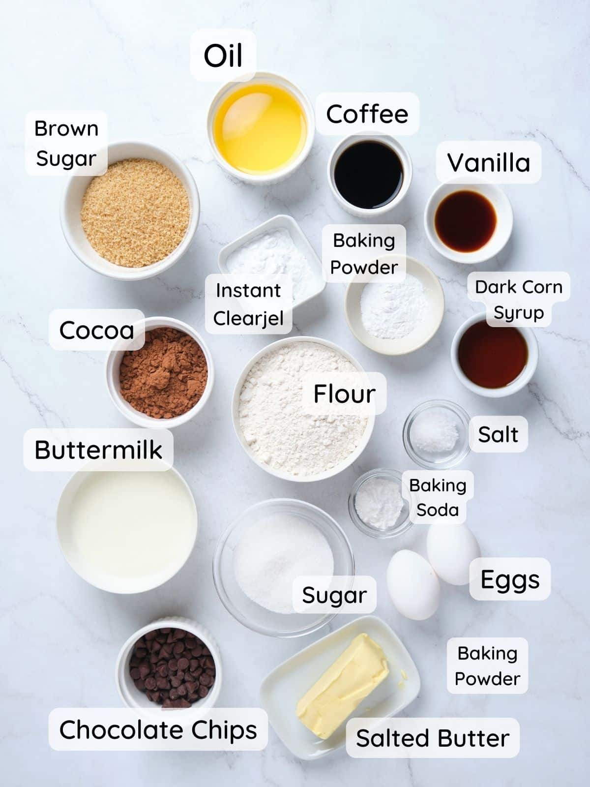 The chocolate fudge cake ingredients on a table with text overlay of "buttermilk, eggs, vanilla, dark corn syrup, butter, sugar, brown sugar, instant clearjel, baking powder, baking soda, salt, cocoa."