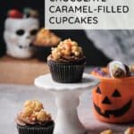 Caramel filled cupcakes topped with a caramel corn topping with Halloween decorations in the background, with the text "dark chocolate caramel filled cupcakes" and "amycakesbakes.com."