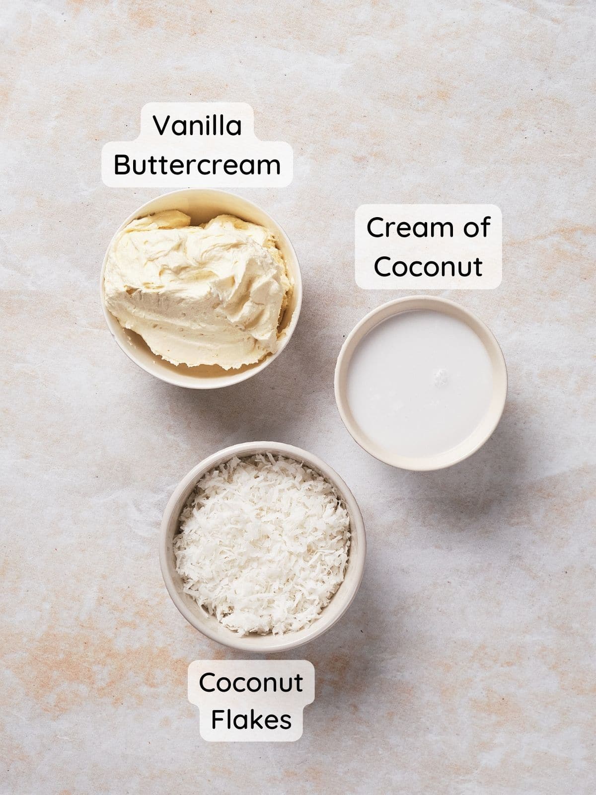 An overhead shot of prepared buttercream frosting, cream of coconut in a bowl, and shredded coconut flakes.