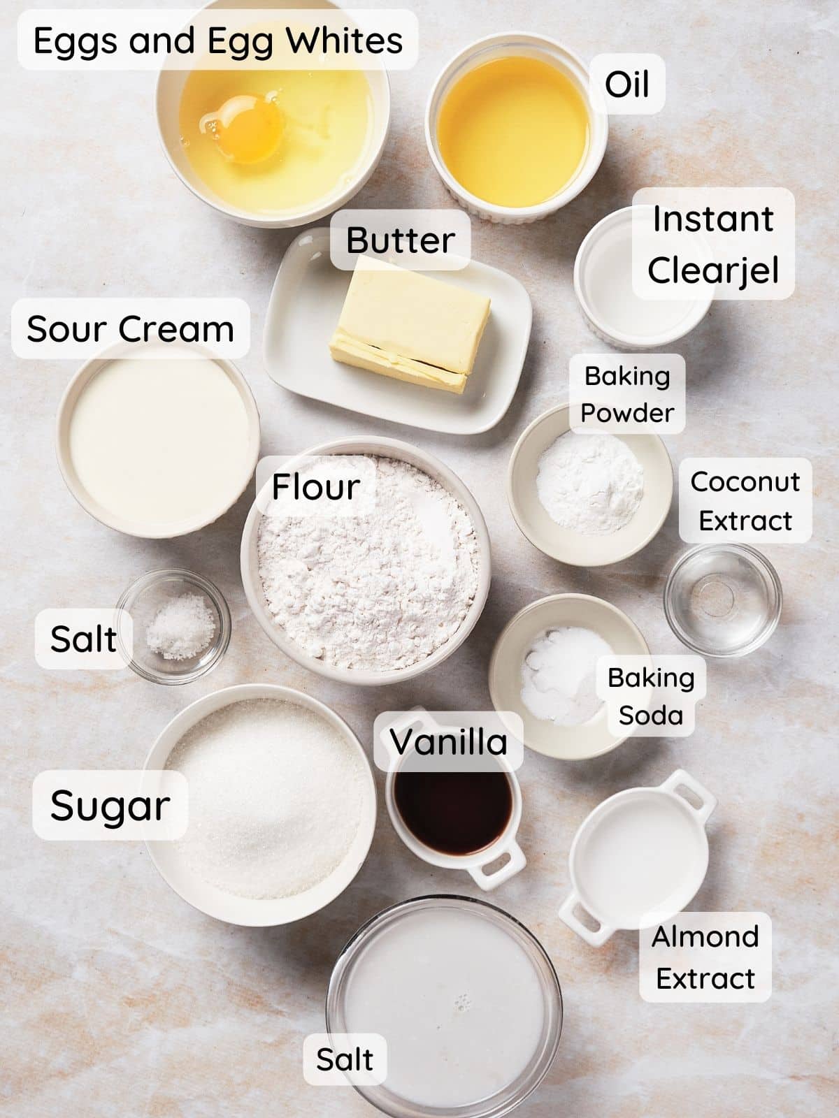 An overhead shot of the coconut cake ingredients, with the text "flour, sugar, baking powder, baking soda, salt, instant clearjel, sour cream, vanilla, almond extract, coconut extract, egg and egg whites, and butter."