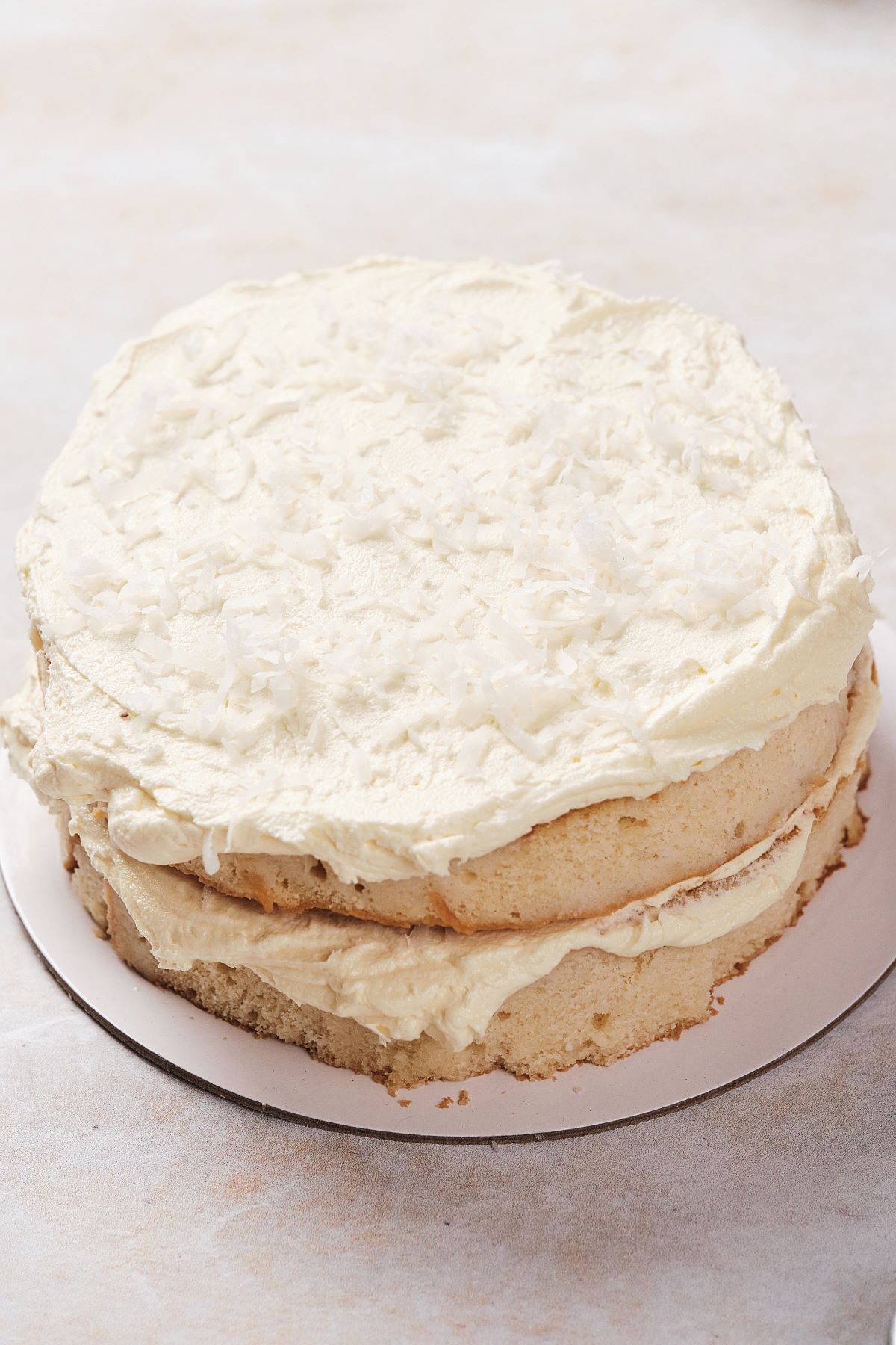 Two layers of the coconut cake being layered with vanilla buttercream and coconut flakes.