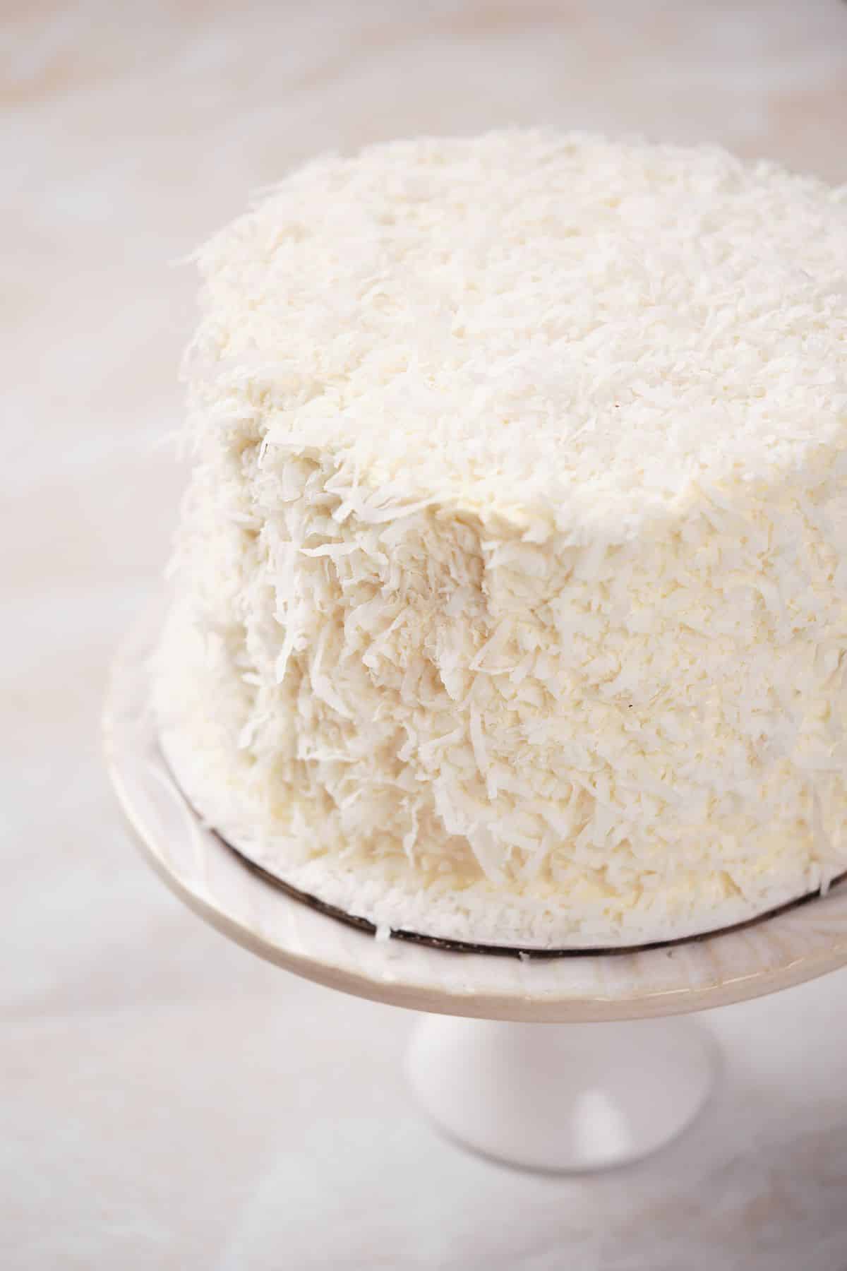 A coconut layer cake covered in coconut flakes.