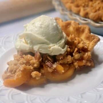 A slice of peach pie with a crumble topping on a plate.