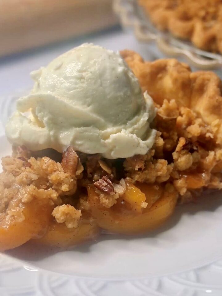 A slice of peach pie with a crumble topping on a plate.