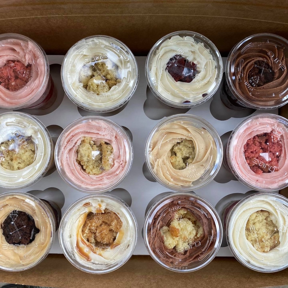 overhead view of a box of mini cake cups in a variety of flavors and toppings.