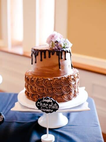 two tiered chocolate fudge wedding cake on a cake stand with a chocolate ganache drip.