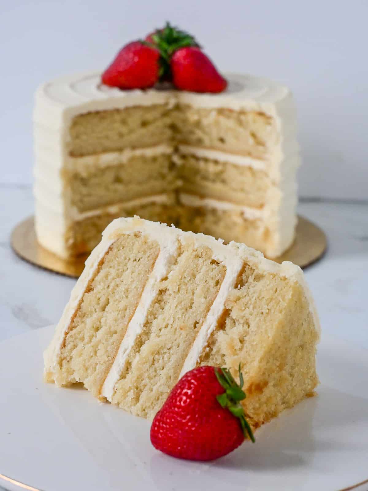 close up view of a slice of vanilla cake made using the reverse creaming method with vanilla buttercream and strawberries for decoration.