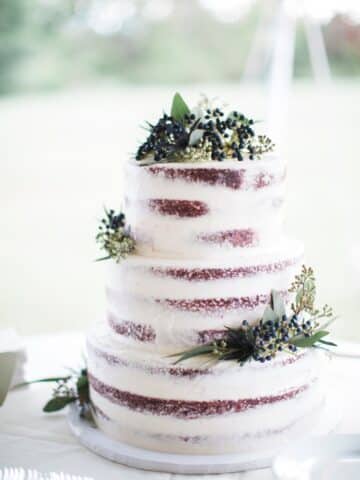three layered wedding cake made with red velvet cake and naked frosting with fresh herbs and flowers for decor.
