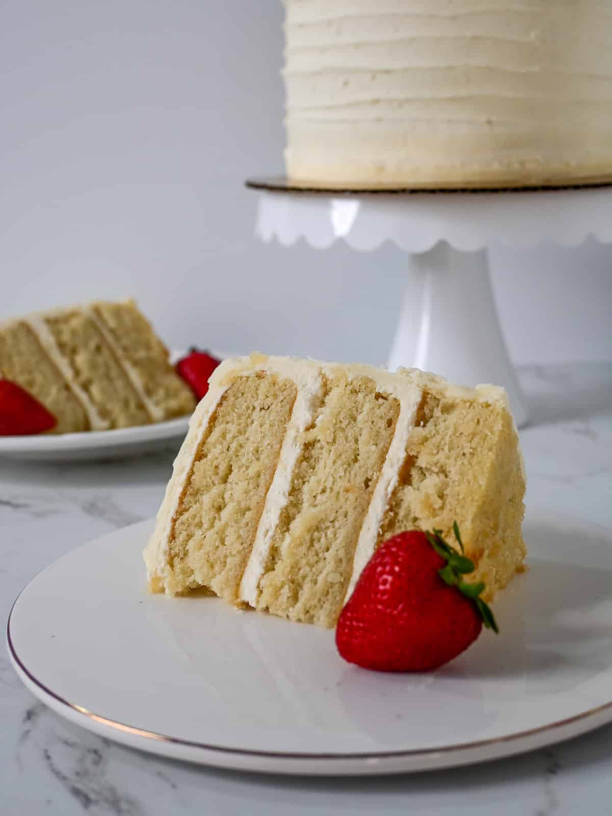 two plates with vanilla white cake in front of a cake stand.