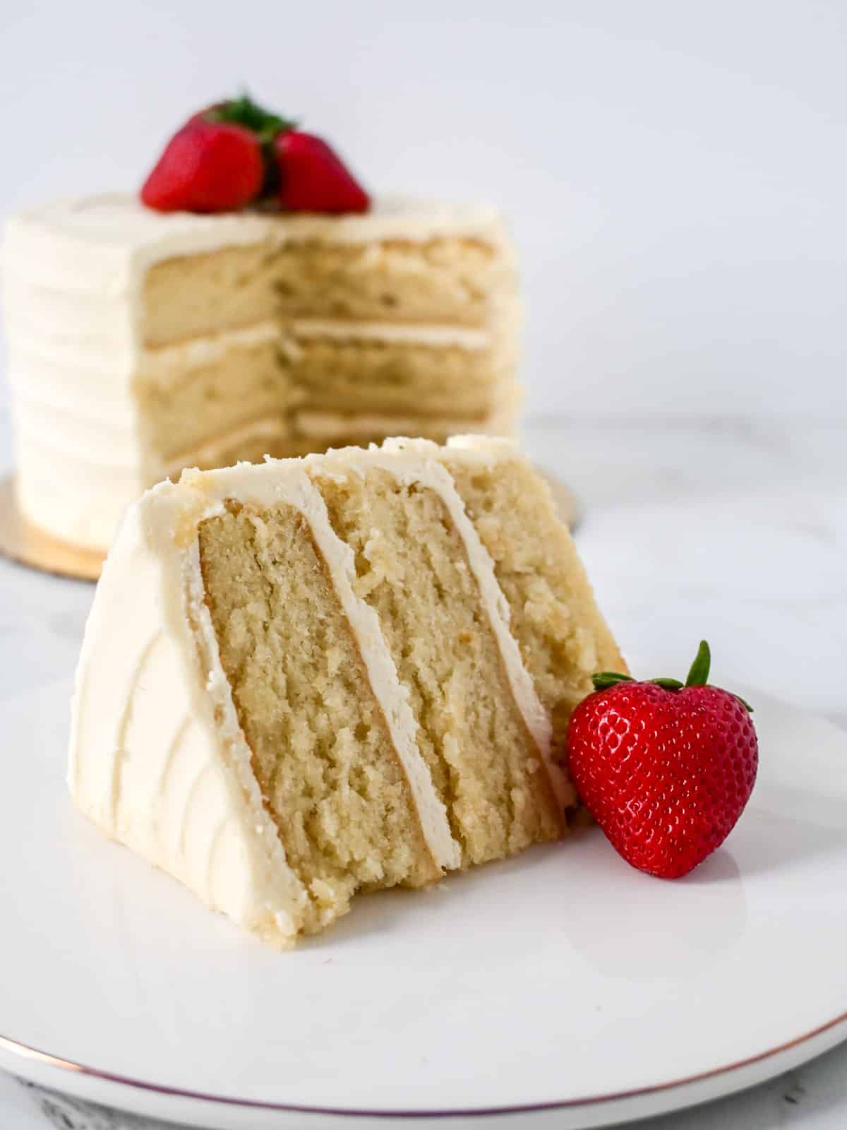 slice of vanilla cake made using the reverse creaming method in front of the layered cake.