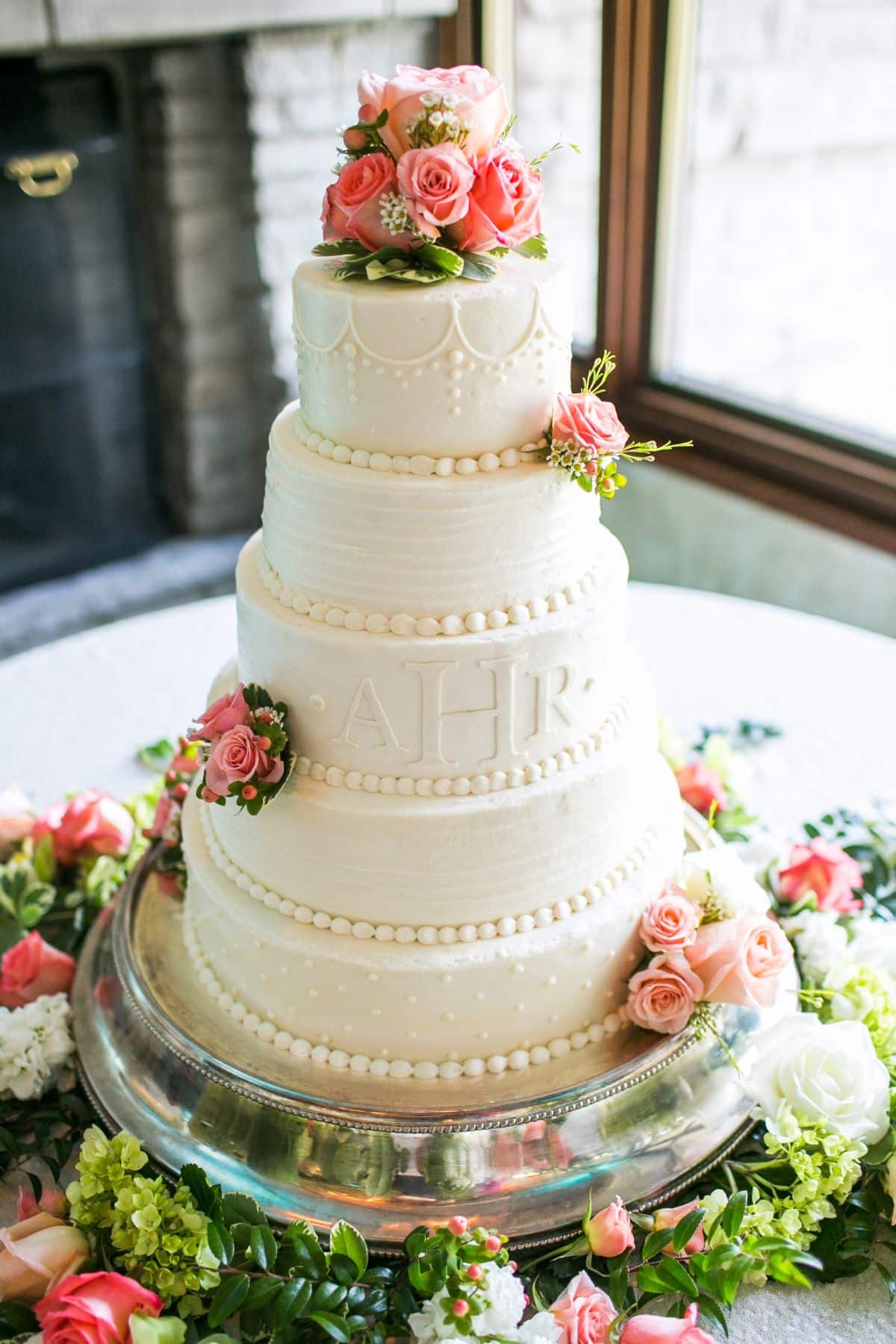 very feminine all white wedding cake with five layers, embossed initials, decorative piping, and miniature pink roses. 
