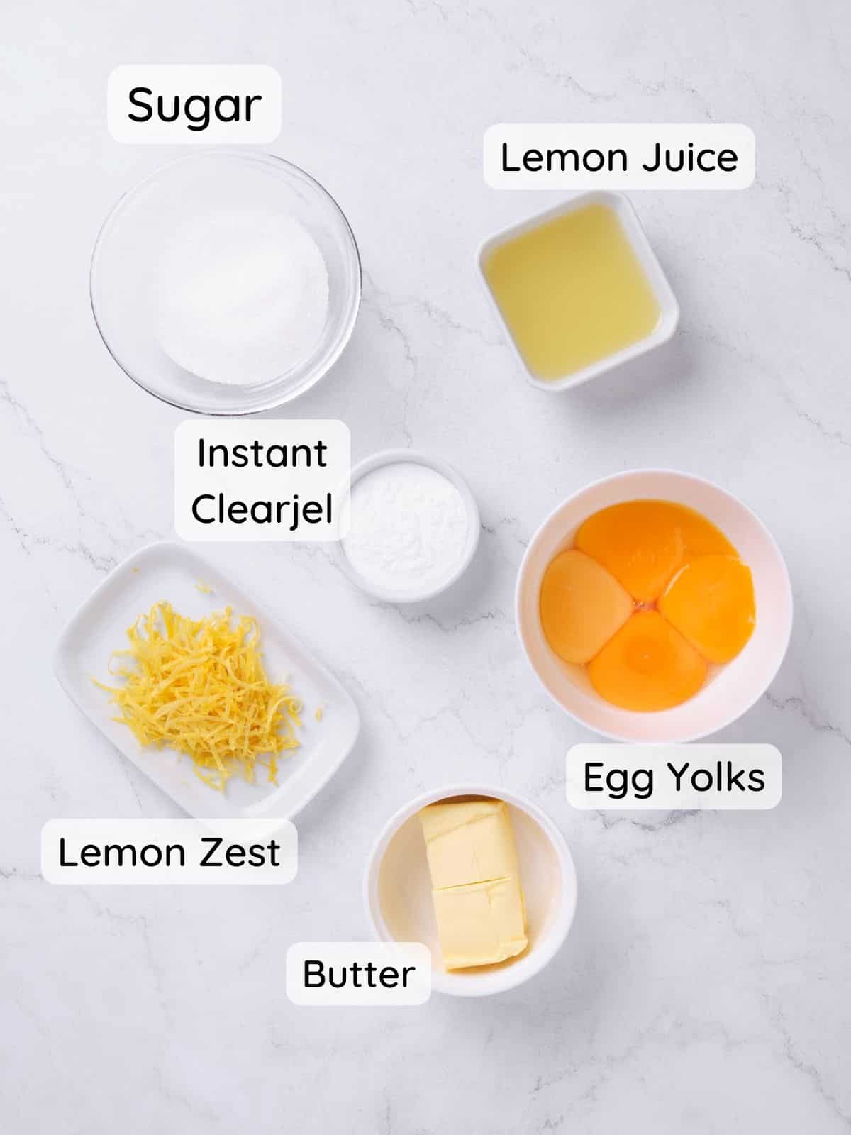 ingredients to make lemon curd cake filling on a marble surface, including sugar, instant clearjel, egg yolks, lemon juice and zest, and butter.