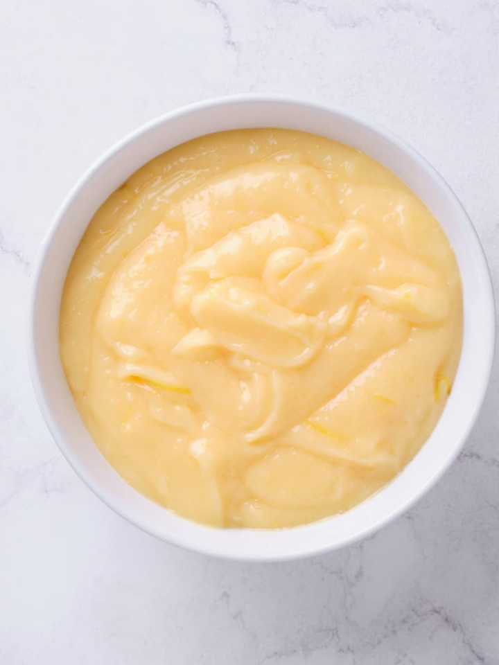 overhead view of a white bowl containing homemade lemon curd on a marble surface.