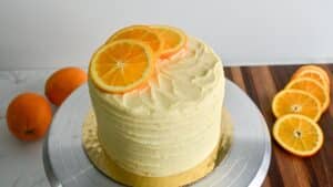 A layer cake with a textured orange buttercream frosting, topped with fresh orange slices.