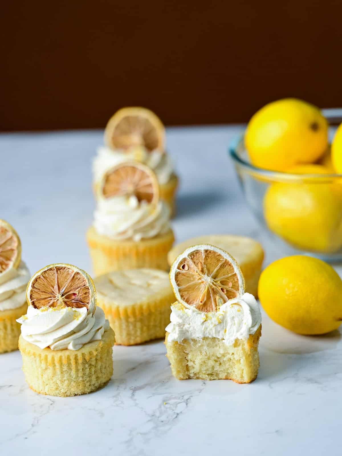 batch of lemon drizzle cupcakes with lemon frosting and dried lemon slices on top.