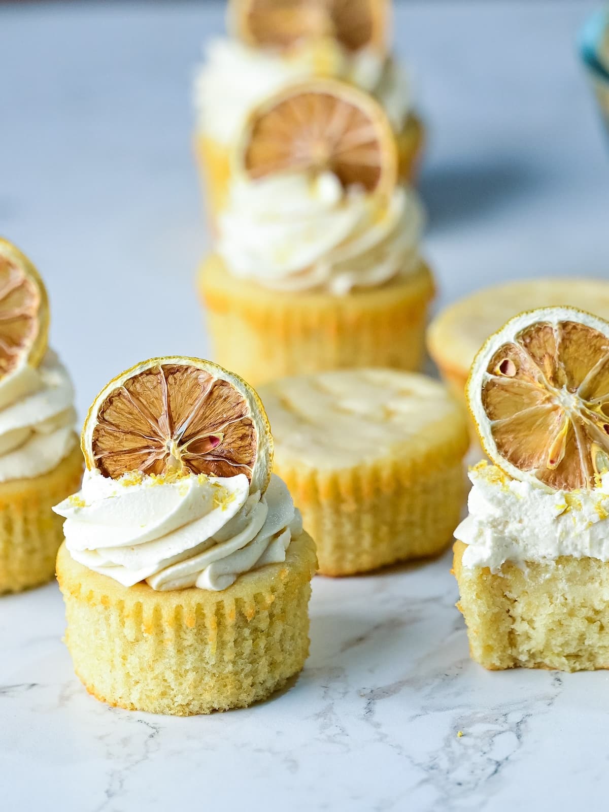 several lemon drizzle cupcakes arranged on a marble surface together.