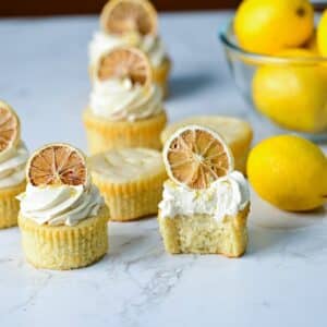 moist lemon drizzle cupcakes on a marble surface with lemon buttercream and dried lemons.