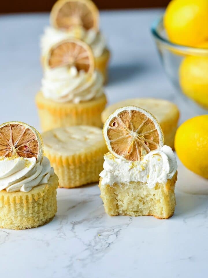 moist lemon drizzle cupcakes on a marble surface with lemon buttercream and dried lemons.