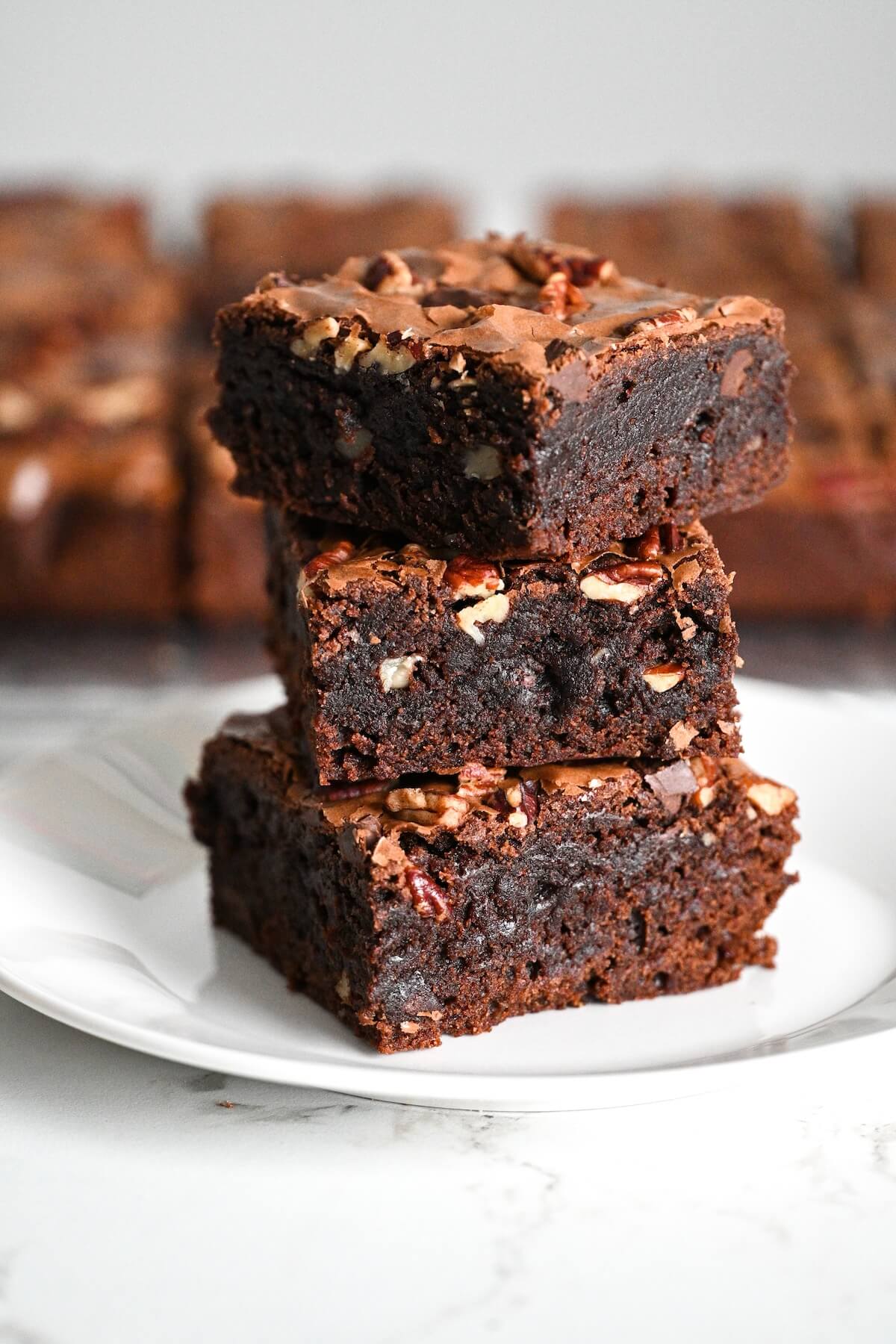 close up of a tower of chewy bakery style brownies with pecans on a white plate.