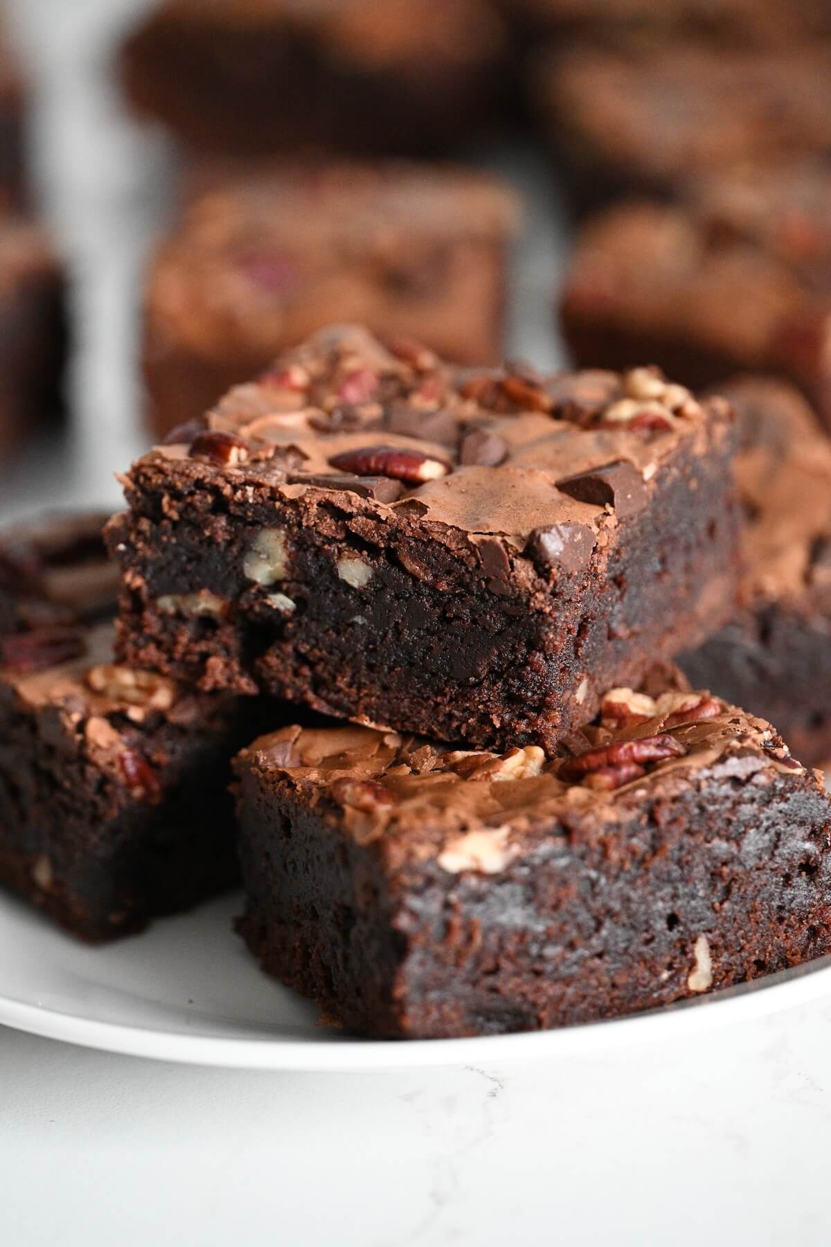 chewy bakery brownie recipe with pecans and boxed mix stacked on a white plate.