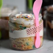 plastic jar with layered cake with a pink spoon taped to the container.