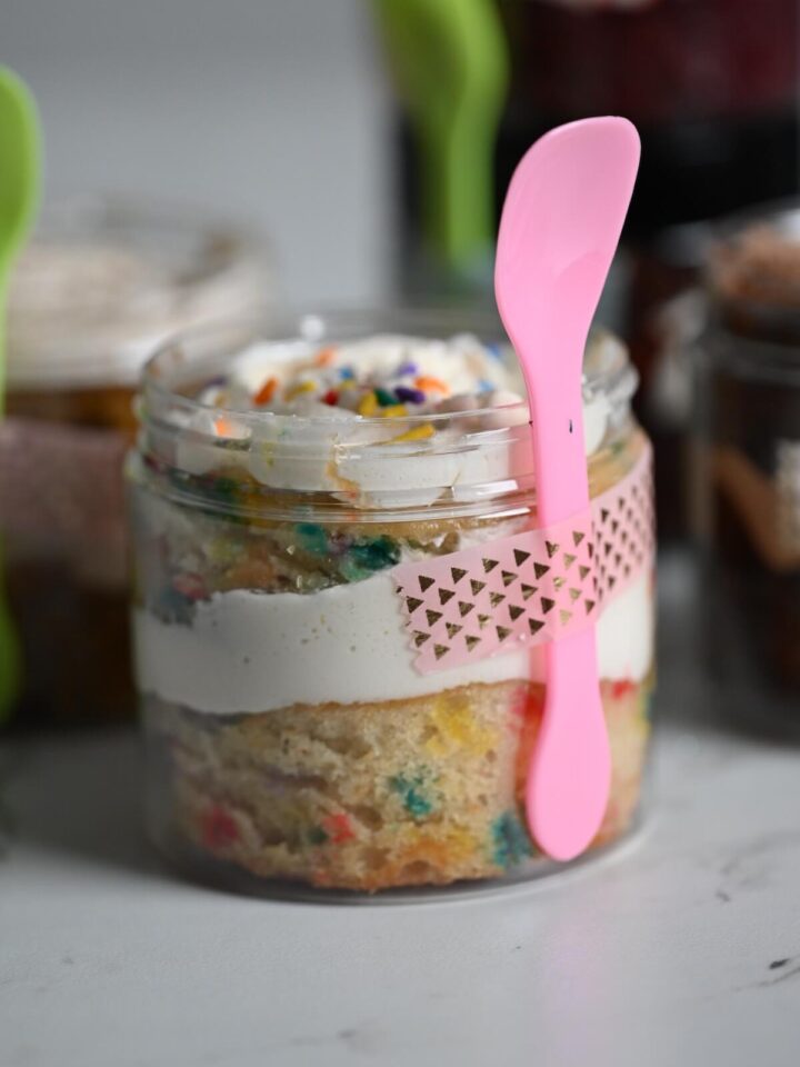 plastic jar with layered cake with a pink spoon taped to the container.
