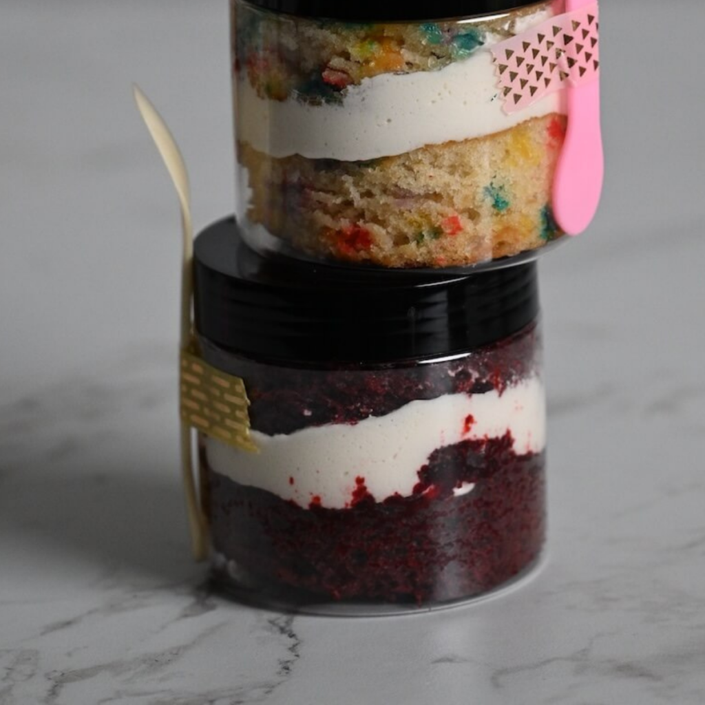 layers of red velvet cake and cream cheese frosting in a plastic jar for easy serving.