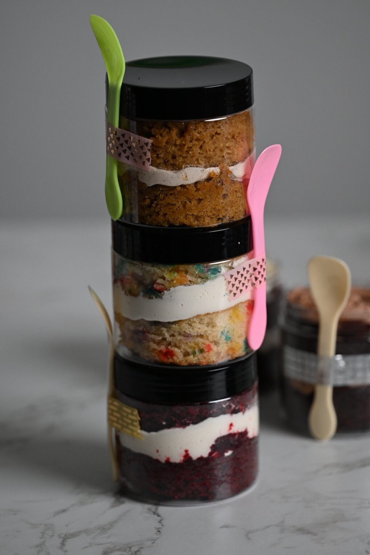 tower of stacked cakes in jars with different flavors, like chocolate cake, red velvet cake, funfetti cake, and carrot cake.