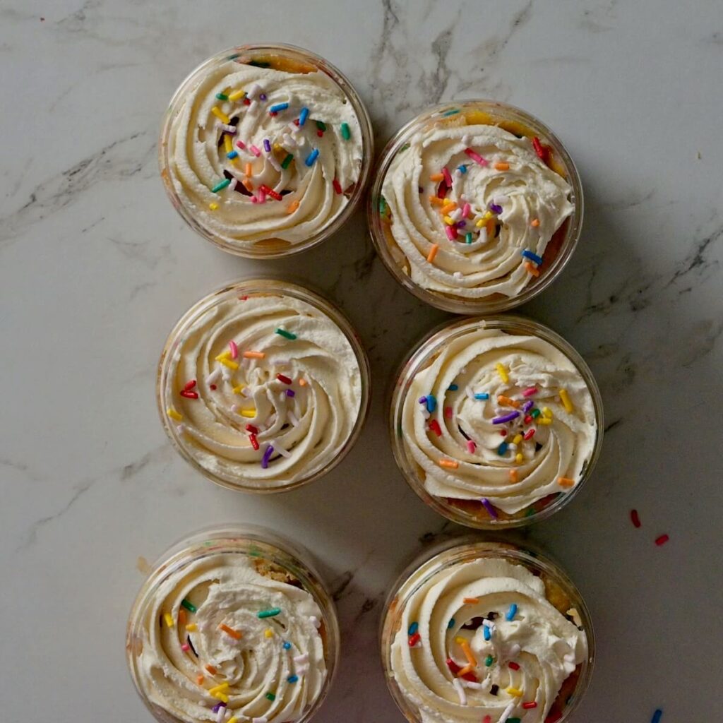 cakes in a jar with frosting and sprinkles on top before closing and adding the small spoon.