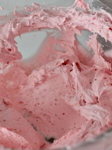 overhead view of a mixing bowl with fresh raspberry buttercream with cream cheese and raspberry extract.