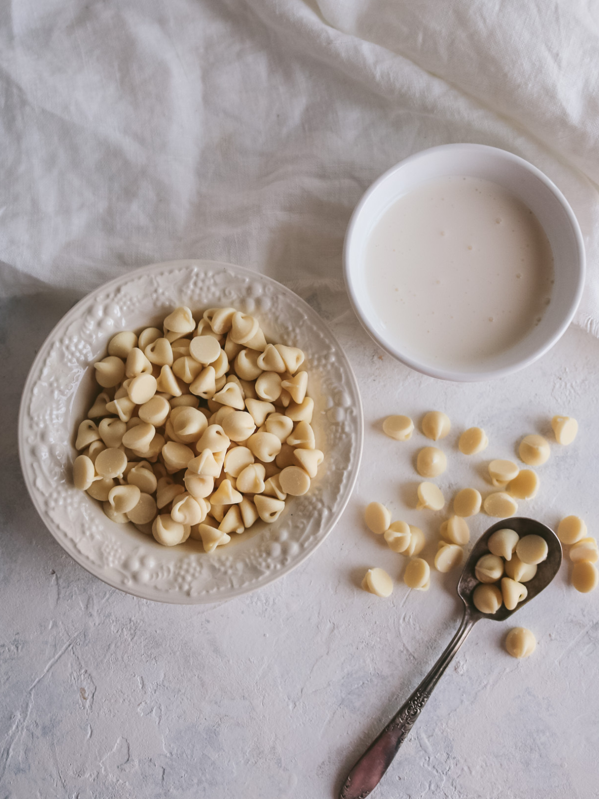 overhead view of a small bowl of white chocolates and a cup of heavy cream to make white chocolate ganache.