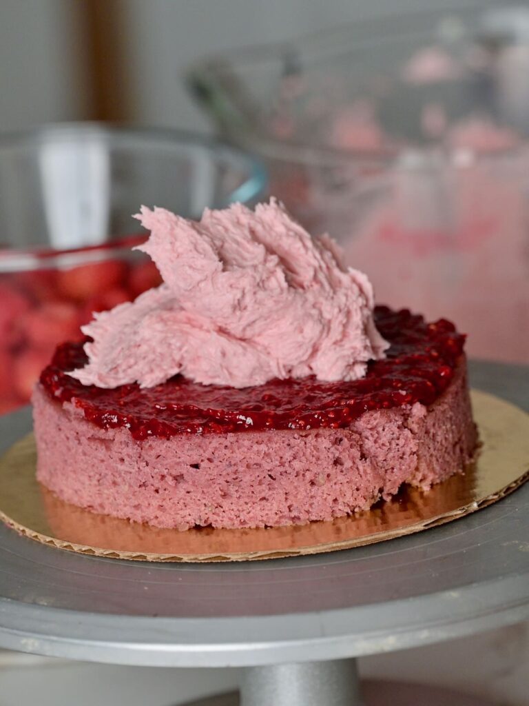 close up view of assembling fresh raspberry cake with the cake layer, raspberry compote, and raspberry buttercream on top.