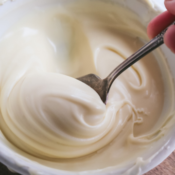 close up view of a spoon scooping up thick white chocolate ganache in a white bowl.
