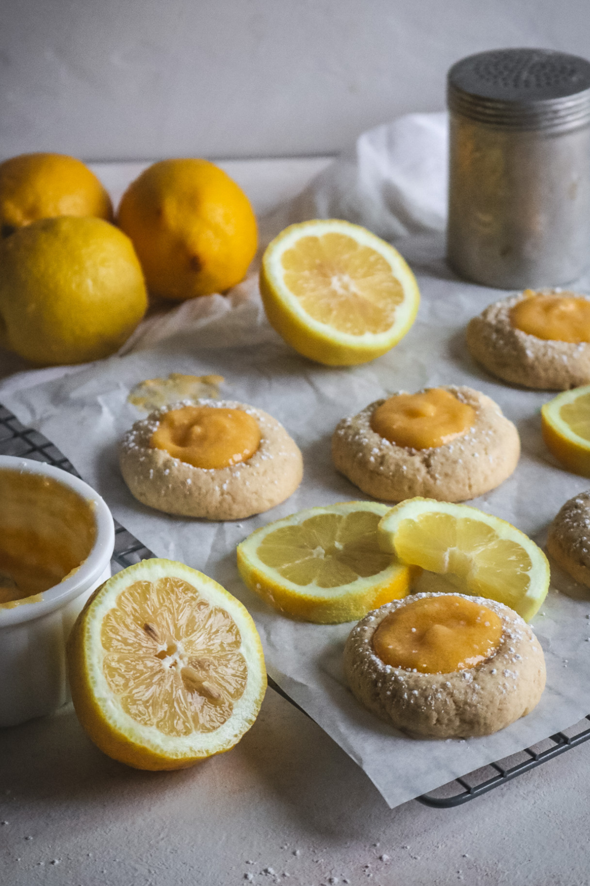 wire rack with parchment paper and fresh lemon curd thumbprint cookies next to sliced lemons.