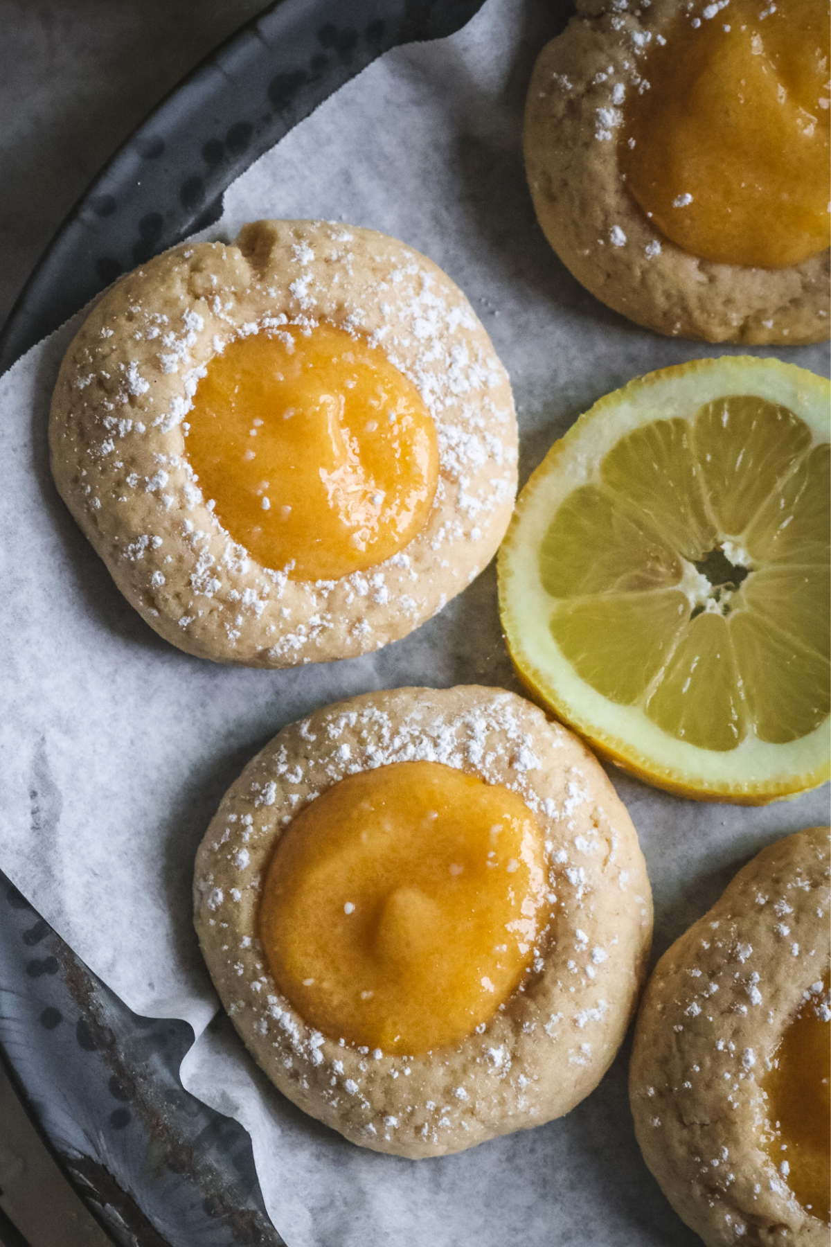 overhead view of chewy lemon curd thumbprint cookies on a gray pie plate lined with parchment paper.