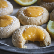 close up view of lemon curd thumbprint cookies on a metal tray with a bite taken out of one of them.