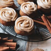 close up view of frosted snickerdoodles on a wire rack next to cinnamon sticks.
