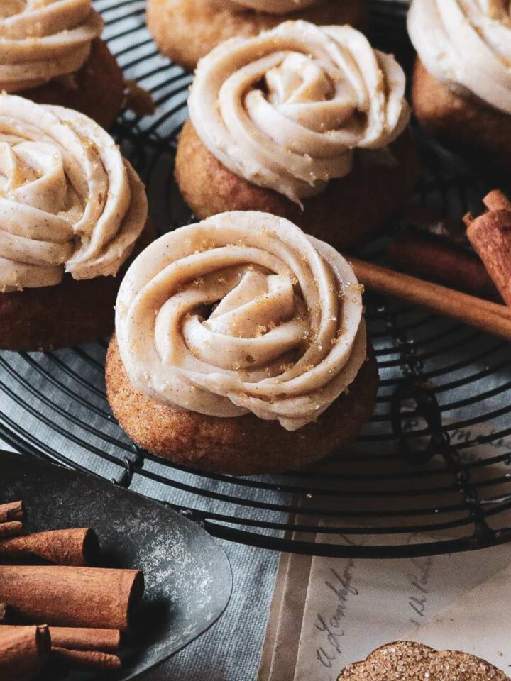 close up view of frosted snickerdoodles on a wire rack next to cinnamon sticks.