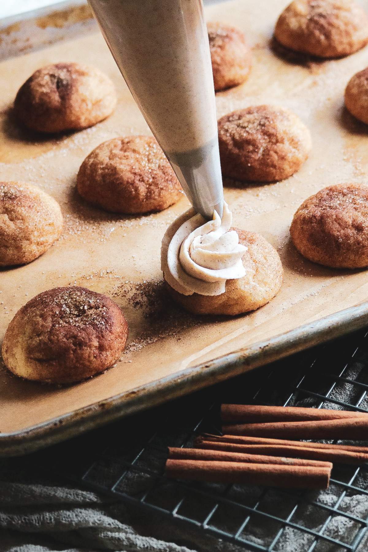piping cinnamon buttercream onto snickerdoodles on a sheet pan.