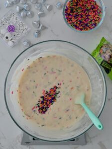 Mixing colorful Halloween jimmies into cupcake batter with a spatula.