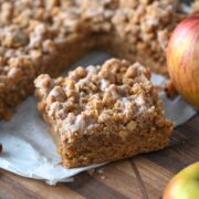 slice of moist applesauce crumb cake on parchment paper next to the rest of the cake and fresh apples.