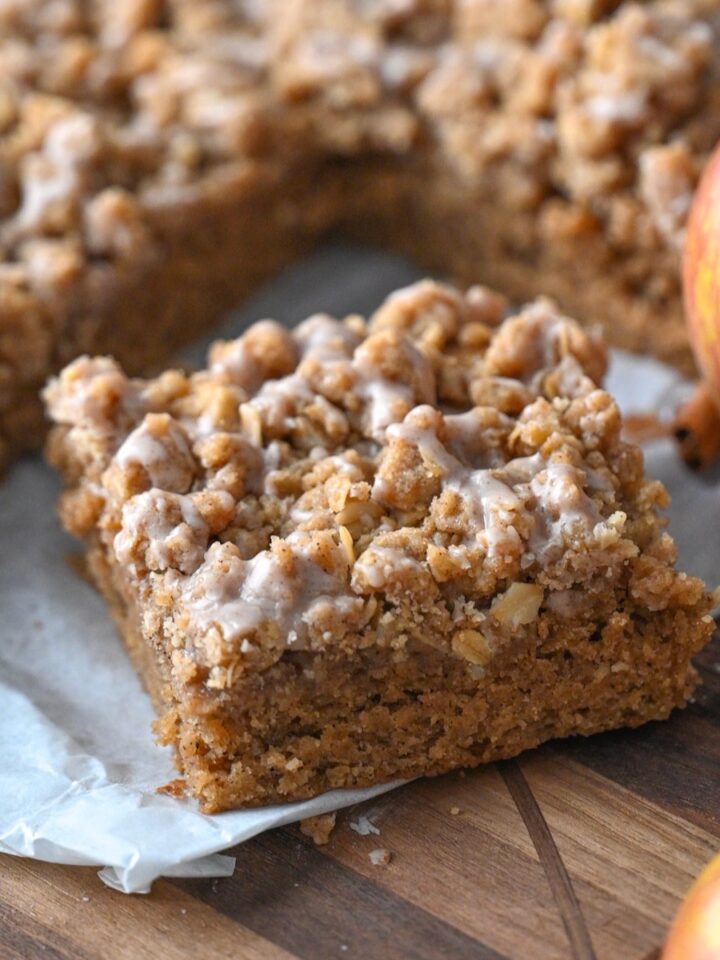 slice of moist applesauce crumb cake on parchment paper next to the rest of the cake and fresh apples.