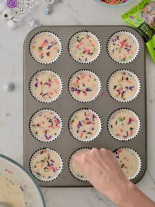 Halloween funfetti cupcake batter with sprinkles on top foil cupcake liners in a 12-count muffin pan.